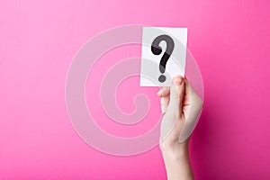 Woman holding card with question mark on color background. Paper note with question mark or sign on pink background. Ask or b