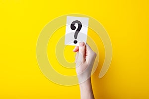 Woman holding card with question mark on color background. Paper note with question mark or sign on yellow background. Ask or b