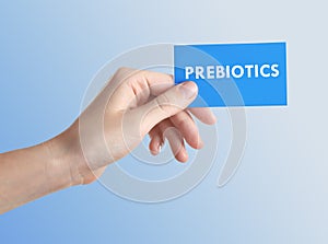 Woman holding card with word PREBIOTICS on light blue background, closeup photo