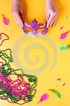 Woman holding carnival mask on bright yellow background, top view, copy space. Border with traditional Mardi gras beads, masks,