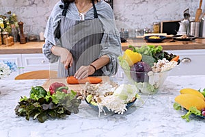 woman holding carrot with kitchen knife on cutting board in kitchen. Chef cuts the vegetables into meal food