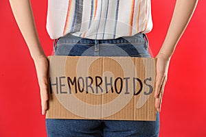 Woman holding carton sign with word HEMORRHOIDS on red background, closeup