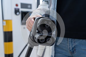 Woman holding CCS fast charging socket type 2 plug for electric vehicles at EV car charging station.