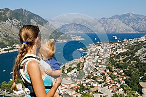 Woman holding child and looking at the mountains and the Bay of Kotor in Montenegro at the top of the mountain. Rear view.