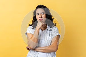 Woman holding chin and musing, looking away with thoughtful facial expression.