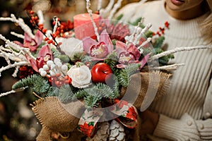 Woman holding a christmas composition with pink orchids, white roses, fir-tree branches, red apple and candle in the