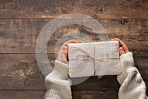 Woman holding christmas gift box. Wooden rustic table. Top view woman hands holding present box