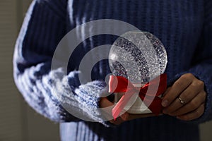 Woman holding Christmas snow globe with red bow, closeup.