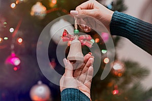 Woman holding christmas tree wooden toy in her hands and hanging it on the Christmas fir tree. Winter holidays lights and garlands