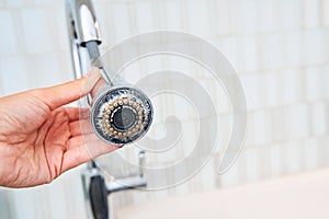 A woman is holding a chrome faucet covered with lime scale