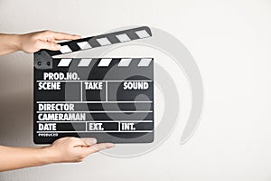 Woman holding clapperboard against light wall, closeup. Cinema production