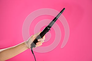 Woman holding clipless curling hair iron on pink background, closeup
