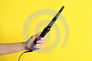 Woman holding clipless curling hair iron on yellow background, closeup