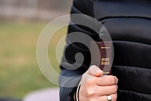 Woman holding closed holy bible book with golden text in hand, close-up