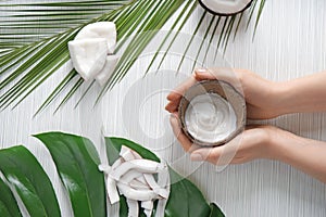 Woman holding coconut bowl with body cream on light background