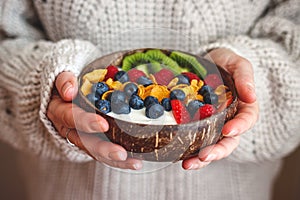 Woman holding coconut bowl with yogurt, corn flakes, sliced kiwi and berry fruit