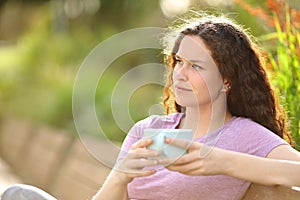 Woman holding coffee contemplating in a park