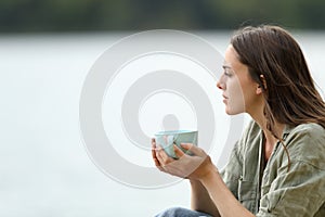 Woman holding coffee cup contemplating a lake