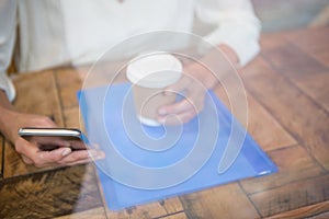 Woman holding coffee cup and mobile phone seen through cafe window