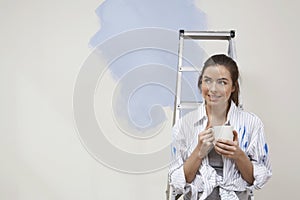 Woman Holding Coffee Cup Next To Stepladder Against Unrenovated Wall