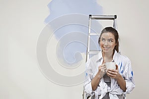Woman Holding Coffee Cup Next To Stepladder Against Unrenovated Wall photo