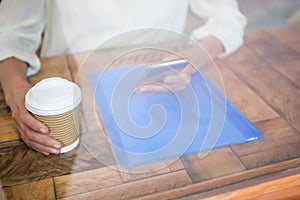 Woman holding coffee cup and smart phone seen through cafe window