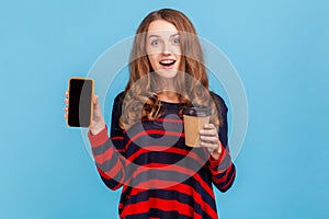Woman holding coffee to go and showing smart phone with blank screen for advertisement.