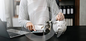 Woman holding coins putting in glass with using smartphone and calculator to calculate concept saving money for finance accounting