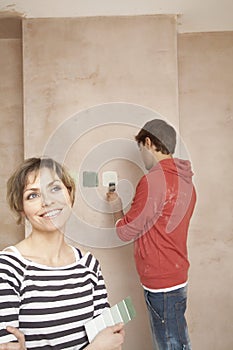 Woman Holding Color Swatches With Man Painting Wall