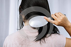 Woman holding comb brushing her hair having problem with hair loss falling on back and shoulder