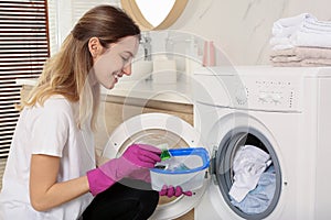 Woman holding container with laundry detergent capsules near washing machine indoors