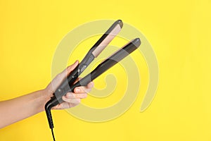 Woman holding corrugated hair iron on yellow background, closeup