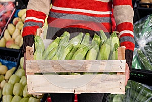 Woman holding crate of zucchini at the market