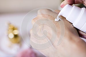 Woman holding cream tube and applying moisturizer cream on her beautiful hands for clean and soft skin. White background. Take