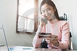 Woman holding credit card and confirm purchase via telephone call to customer service, smiling asian girl making payment