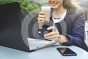 woman holding credit card in hand and using laptop while drinking coffee at cafe. online shopping and payment concept