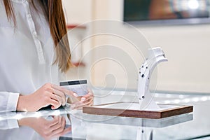 Woman is holding credit card in her hands and standing near the necklace in a jewelry shop.