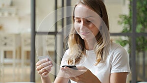 Woman holding credit card and smartphone. Young woman sitting on sofa spend money at home, make order, buying using