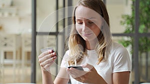 Woman holding credit card and smartphone. Young woman sitting on sofa spend money at home, make order, buying using