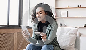 Woman holding credit card and using mobile phone at home, businesswoman shopping online