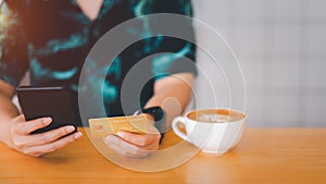 Woman are holding credit card and using mobile phone to pay for online shopping in a coffee shop.