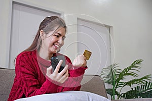 Woman holding credit card and using smartphone at home, online shopping, online banking, payment, spending money, e