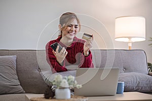 Woman holding credit card and using smartphone at home, online shopping, online banking, payment, spending money, e