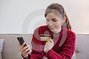 Woman holding credit card and using smartphone at home, online shopping, online banking, payment, spending money, e