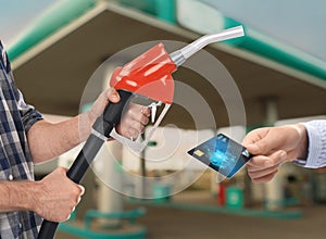 Woman holding credit card and worker with fuel nozzle at gas station, closeup. Cashless payment