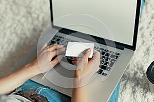 Woman holding credit card and working on a laptop Female using a laptop sitting on floor