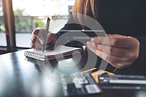 A woman holding a credit card while writing down on notebook on table