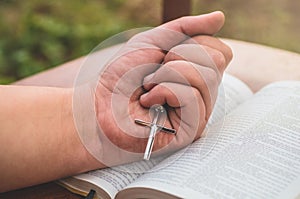 Woman holding a the cross in hand against the background of the bible.