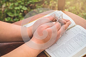 Woman holding a the cross in hand against the background of the bible.