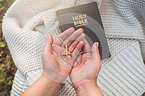 Woman holding a the cross in hand against the background of the bible.